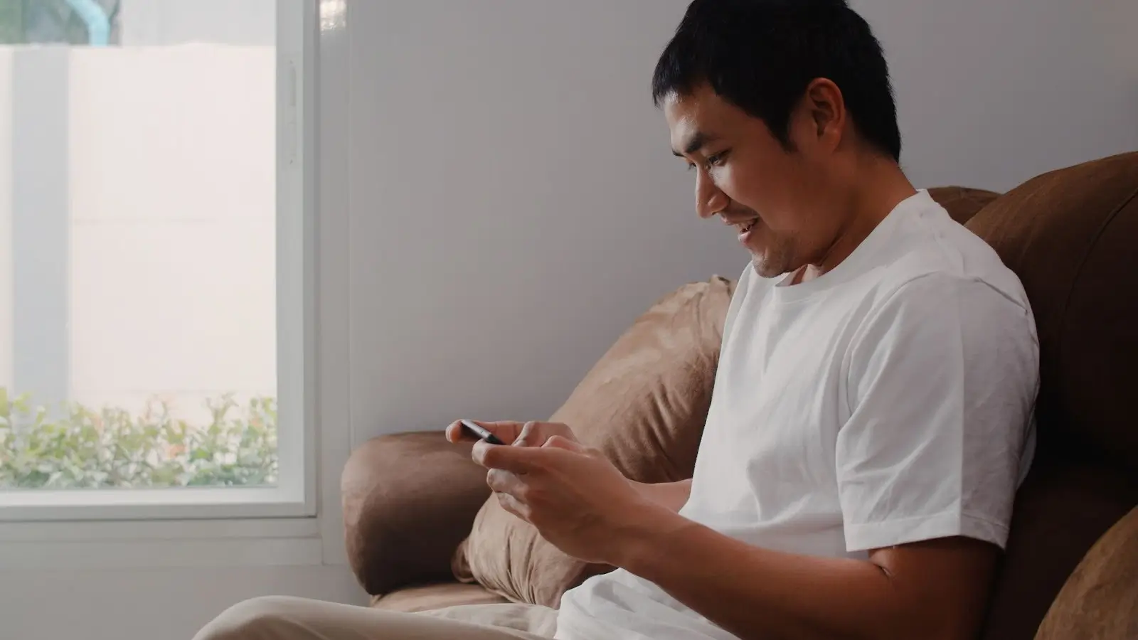A relaxed man using his mobile phone at home represents how players calmly evaluate casino bonuses and Chinese New Year (CNY) promotions before deciding whether to join an online casino Malaysia platform like Winbox.